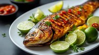 Grilled whole fish with lime slices and herbs on white plate. Fresh seafood dinner with citrus garnish and spicy sauce. Restaurant quality meal presentation.