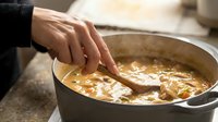 Hand stirring homemade soup in pot with wooden spoon. Cooking healthy meal preparation in kitchen. Warm comfort food being prepared for dinner.