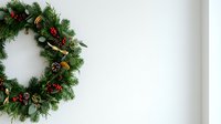 Festive evergreen wreath with red berries, pinecones, and gold ribbon bow on white wall background for holiday decorations and seasonal greeting cards.