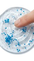 Finger touching clear gel with blue beads and exfoliating particles, isolated on white background for skincare product design and cosmetic packaging applications.