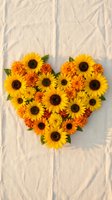 Heart-shaped arrangement of yellow sunflowers and orange marigolds on rustic wooden background for autumn wedding decor and romantic greeting cards.