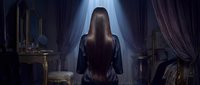 Young woman with long brown hair in dark dress standing by window with dramatic light beam in vintage bedroom interior for storytelling concepts.