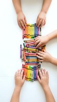 Children hands reaching for colorful crayons arranged in rainbow pattern on white background for creative art education and learning activities.