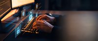 Hands typing on laptop keyboard with glowing digital security icons floating above, representing cybersecurity, data protection and online safety concepts.