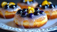 Glazed donut topped with fresh blueberries and lemon zest on decorative white plate, shallow depth of field creates appetizing bakery presentation.