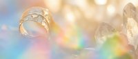 Macro shot of a sparkling water drop and crystal quartz with rainbow light reflections on a soft pastel bokeh background.