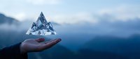 Unrecognizable person holding transparent ice crystal pyramid against misty mountain landscape, symbolizing environmental conservation and sustainability concepts.