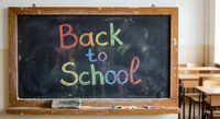 Back to school colorful chalk text on classroom blackboard with wooden frame and desks in background for education and learning concepts.