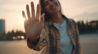 Young Asian woman extending hand toward camera in stop gesture during golden hour sunset by urban waterfront for communication and lifestyle concepts.