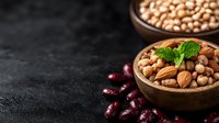 Mixed nuts and legumes in rustic wooden bowl with fresh mint garnish on dark stone background, healthy protein-rich vegetarian snack for balanced nutrition.