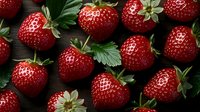 Fresh ripe strawberries with green leaves arranged on dark wooden background, macro food photography showing juicy texture and natural pattern.