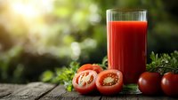 Fresh tomato juice in glass with ripe red tomatoes and herbs on wooden table in natural sunlight for healthy lifestyle and nutrition concepts.