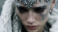 Young woman with dramatic gothic makeup featuring ornate silver face jewelry and dark eye makeup for fantasy costume design.