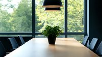 Modern conference room with wooden table, black chairs, potted plant, and pendant light, overlooking green trees through large windows.