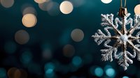 Silver snowflake ornament hanging against dark teal background with warm golden bokeh lights creating festive holiday atmosphere for seasonal decorations.