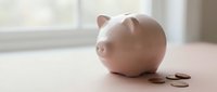 Pink ceramic piggy bank with scattered coins on wooden surface near bright window for savings and financial planning concepts.