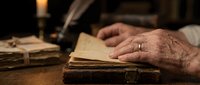 Elderly hands with wedding ring touching vintage leather-bound book by candlelight, creating warm nostalgic atmosphere for reading and literature concepts.