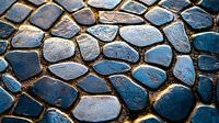 Wet cobblestone pavement with irregular stone shapes reflecting golden sunlight, creating dramatic contrast between dark blue stones and glowing edges. Background for design.