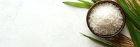 Raw white jasmine rice in wooden bowl with green palm leaves and rice ear on light stone background with copy space for menu or recipe.