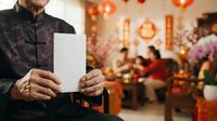 Man holding blank white card at festive gathering with traditional decorations and family members celebrating in background.