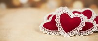 Red fabric hearts with white lace trim arranged on wooden surface for Valentine's Day romantic decoration and craft projects.