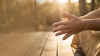 Elderly hands reaching out in warm golden sunlight on wooden deck, symbolizing hope, help, assistance, and human connection in peaceful outdoor setting.