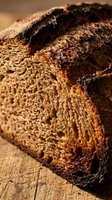 Freshly baked artisan bread loaf with crispy, scored crust and golden-brown exterior on wooden surface. Ideal for bakery, food, and culinary content.