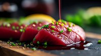 Fresh raw tuna sashimi slices garnished with chopped chives and soy sauce on dark wooden board, close-up view with selective focus in restaurant setting.