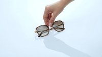 Woman hand holding tortoiseshell sunglasses against light background, summer fashion accessory concept with elegant style and minimalist composition.