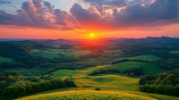 Dramatic sunset over rolling green hills and meadows with vibrant orange sky and dramatic clouds, creating magical countryside landscape at golden hour.
