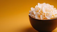 Delicate white jasmine flowers in dark ceramic bowl against warm orange background, creating minimalist Asian spa and wellness atmosphere for relaxation designs.