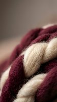 Close-up macro shot of burgundy and cream colored wool yarn fibers showing natural texture and weave detail for crafting and textile projects.