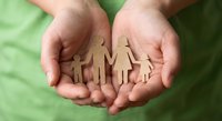 Protective hands holding wooden family figures representing care, support, insurance and social services concept for community welfare programs.
