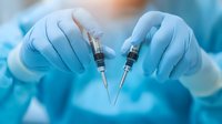Medical professional in blue protective gloves holding two syringes with vaccine or medicine against blurred hospital background, healthcare concept.