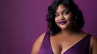 Young African American woman with curly hair and purple lipstick wearing elegant dress against vibrant purple background for fashion and beauty content.