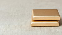 Two golden metallic rectangular bars stacked on neutral linen fabric surface for luxury design projects and premium branding materials.