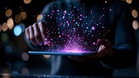 Magical glowing particles burst from tablet screen with hands holding device against dark background with bokeh lights, creating ethereal digital art effect.