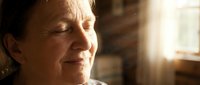 Middle-aged woman with light skin tone and brown hair experiencing emotional distress, tears streaming down face, indoor setting with warm natural light filtering through window, conveying grief, sadness, or difficult life moment.