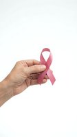 Hand holding pink ribbon symbol for breast cancer awareness campaign isolated on white background for medical and healthcare design.