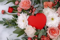 Red heart shape among romantic floral arrangement with pink roses, white chrysanthemums, eucalyptus leaves and coral berries on soft white background.