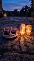 Romantic evening setup with wine glasses and glowing candles on stone patio during twilight hour creating intimate outdoor dining atmosphere.