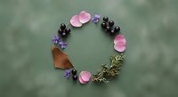 Natural circular wreath arrangement with pink rose petals, purple violets, dark berries and autumn leaf on soft green background for botanical design.
