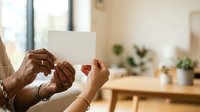 Couple holding blank white card together in modern home interior with natural light and potted plants, expressing love and togetherness for greeting cards and relationship messaging.