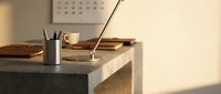 Modern minimalist workspace with wooden desk, sleek lamp, coffee cup and office supplies in warm natural lighting for productivity and focus.
