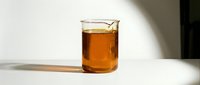 Glass beaker filled with amber liquid, casting shadow on white surface. Laboratory or scientific beverage concept.