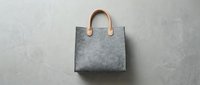 Gray felt tote bag with tan leather handles on neutral background, suitable for fashion, retail, and product design projects.