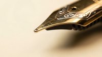 Golden fountain pen nib close-up with ornate engravings on warm beige background for luxury writing and calligraphy projects.