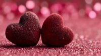 Two sparkling red glittery hearts on shimmering surface with soft pink bokeh lights background for Valentine's Day romance love celebration greeting cards.