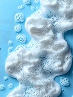 White foamy soap bubbles on bright blue background, creating abstract texture with frothy lather and tiny air bubbles for cleaning concept.