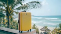 Yellow hardshell suitcase on balcony railing with tropical beach, palm trees and turquoise ocean waves in background, summer vacation travel concept.